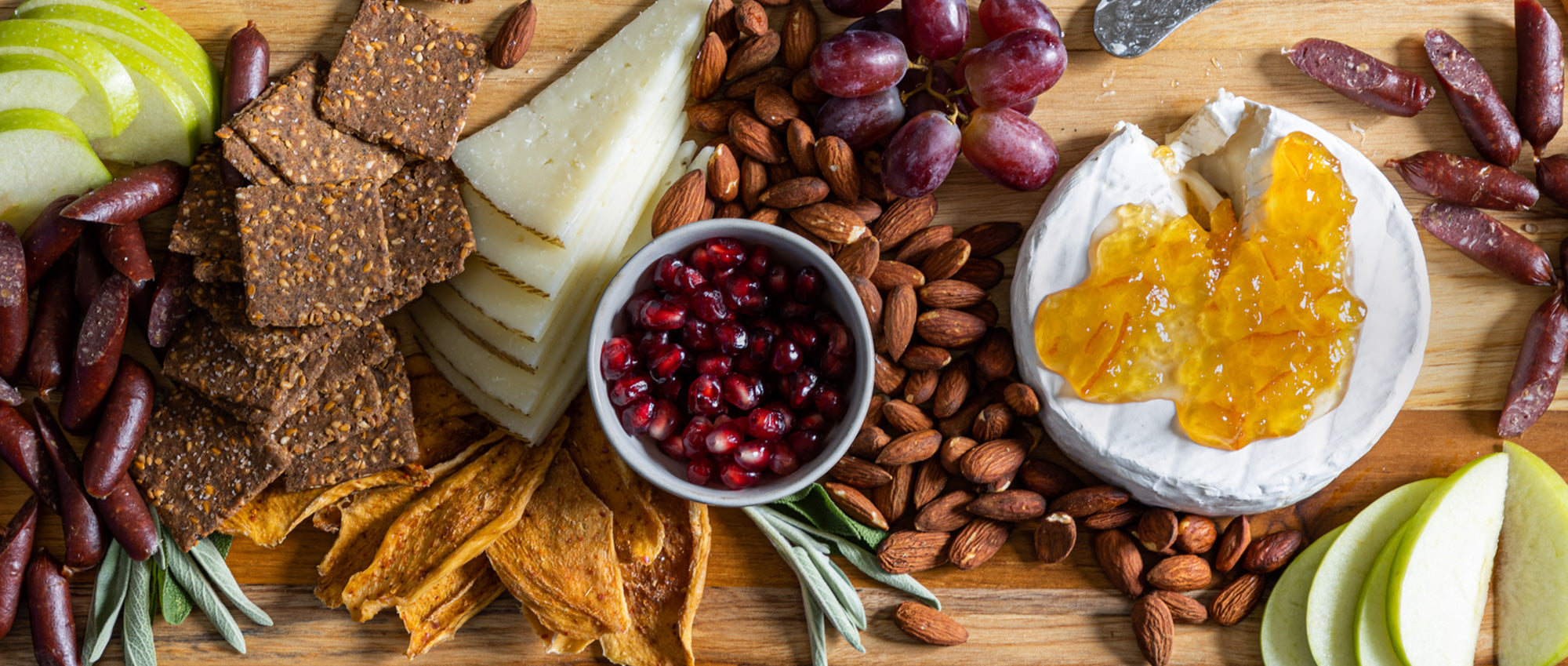 A wooden board covered with crudite for a celebration - Patagonia Provisions breadfruit crackers, sliced fruits, almonds, brie topped with preserves